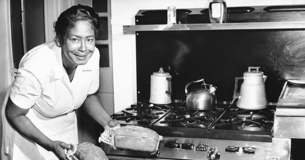 An old black and white photo of a woman in a kitchen.
